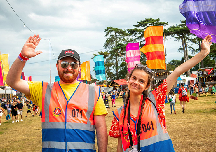 Jobs and Volunteering at Camp Bestival Shropshire 2022 with Hotbox Events - Volunteer stewards waving in main arena - 2022-001 740x521Px72Dpi